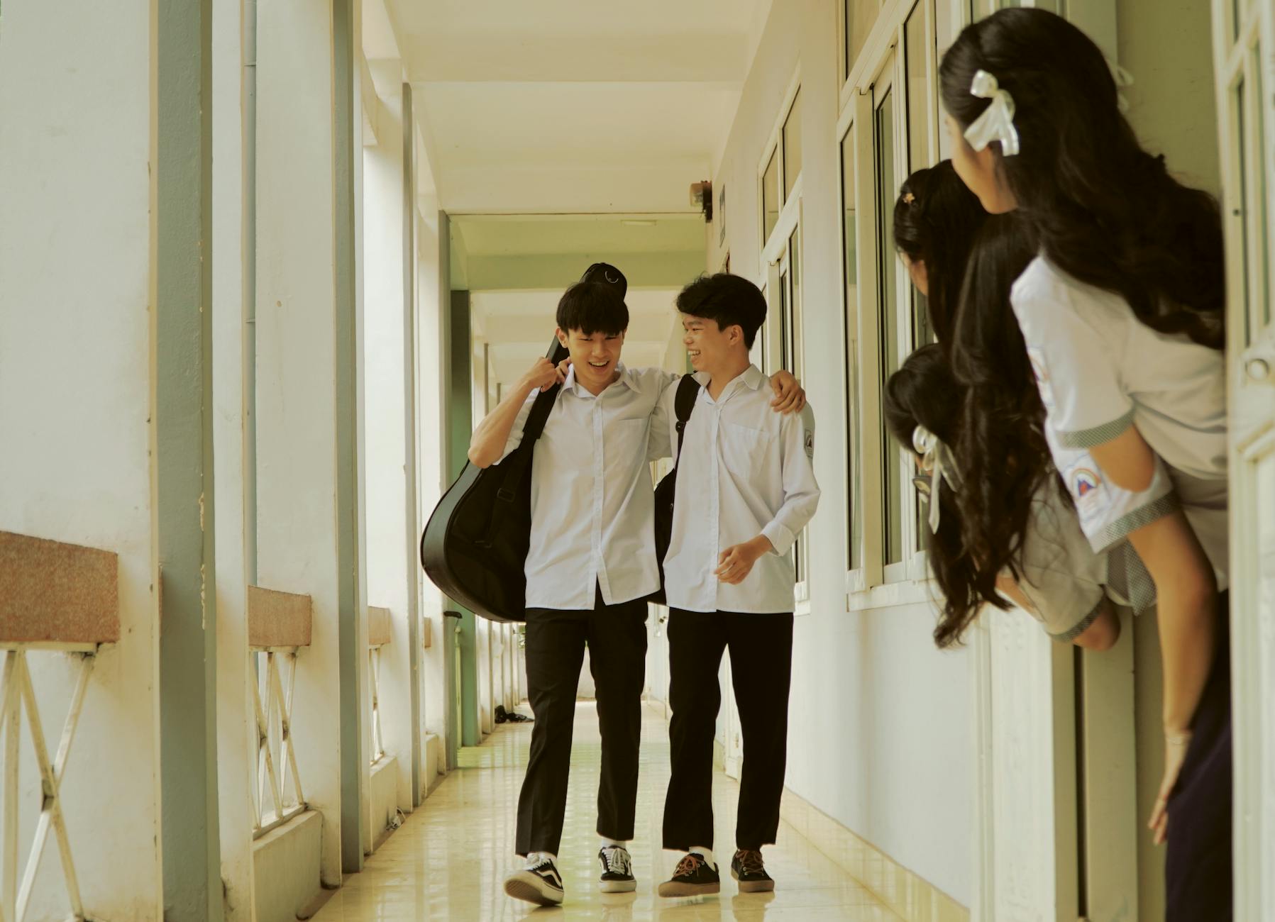 schoolboys walking down the corridor watched by a group of schoolgirls hiding behind the classroom door